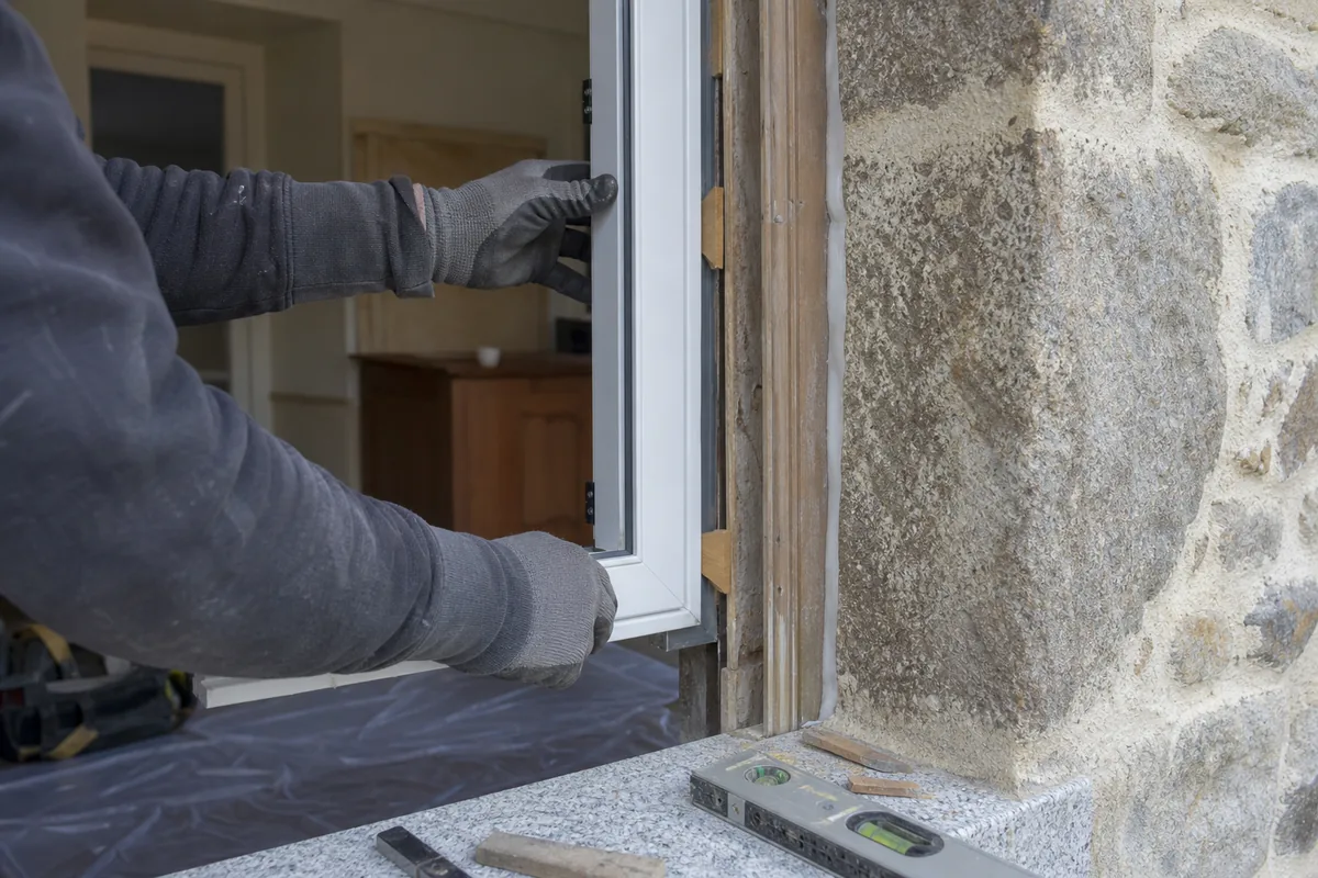 Pose en rénovation d’une fenêtre PVC blanche sur un dormant existant, mains gantées au travail