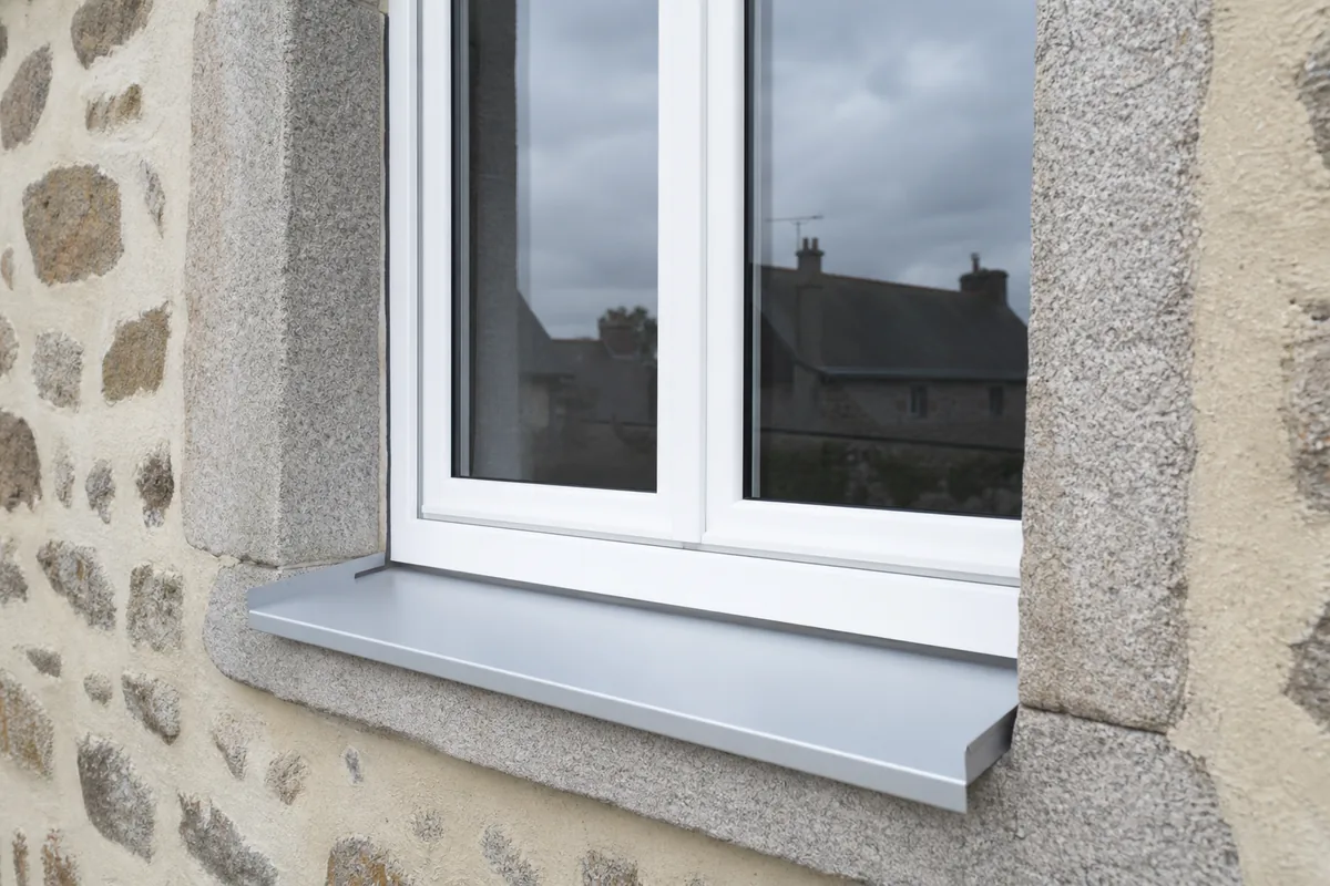 Fenêtre PVC blanche neuve posée dans un encadrement de granit, joints extérieurs finis