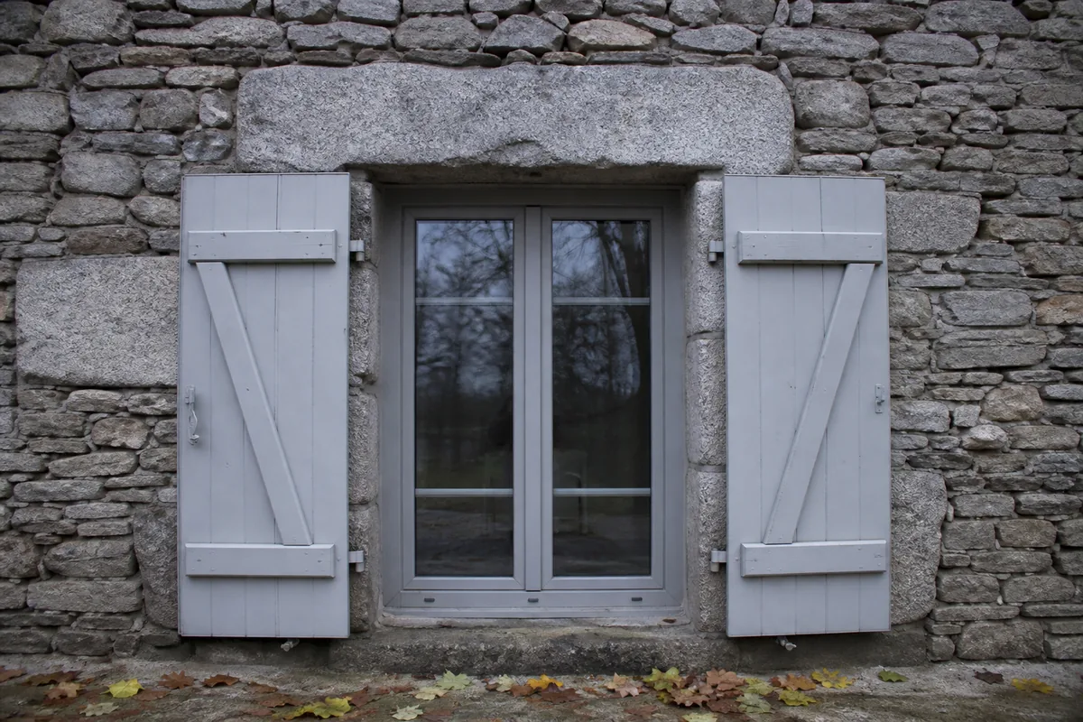 Volets battants gris posés sur une façade en moellon de granit sous une lumière voilée du Limousin